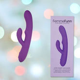 Image of a purple Femme Funn Ultra Rabbit Vibrator, positioned vertically. The product, known for its powerful vibrations and G-spot stimulation, is displayed next to its box, which features an illustration of the vibrator and product details. The background is blurred with soft pastel colors.